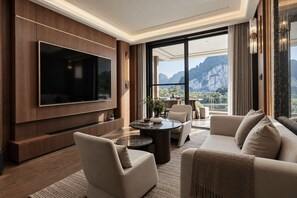 Una sala de estar moderna con un televisor de pantalla plana grande, asientos cómodos, una mesa de centro y vistas a las montañas a través de amplias ventanas.