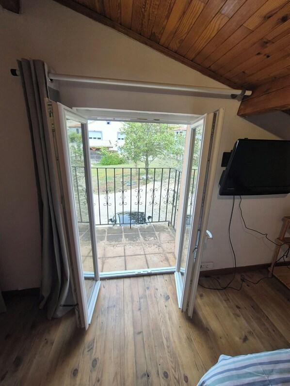 A room with a wooden ceiling, a sliding glass door leading to a patio with a metal fence, and a television mounted on the wall.