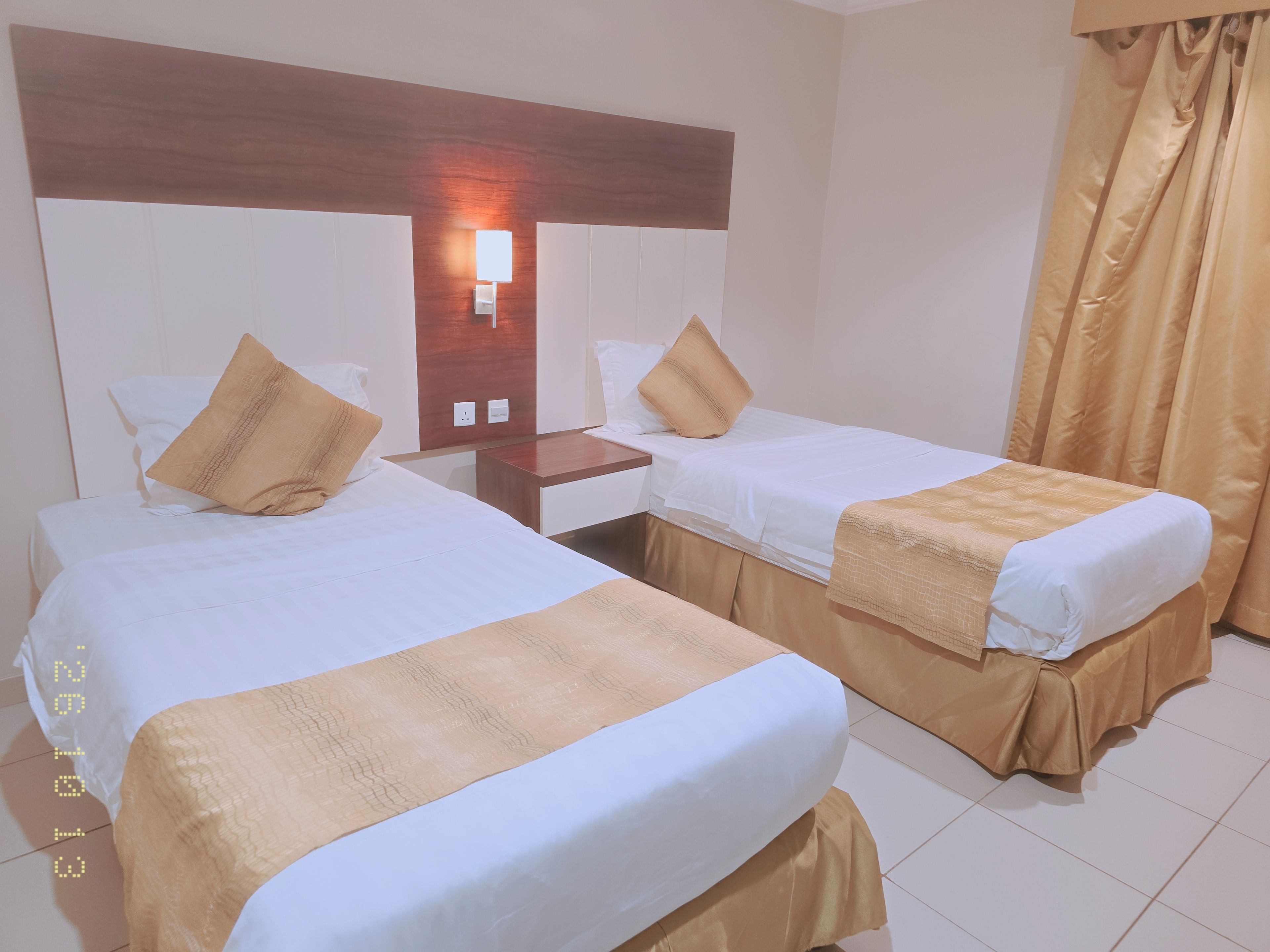 Una habitación de hotel con dos camas, una mesita de noche, una lámpara de pared y una cortina.