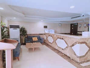 A reception area with a reception desk, a blue sofa, a coffee table, and a potted plant. - jumayra layn (jedda)