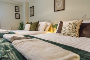 A hotel room with two beds, each with a different pillow design, a green throw blanket, and framed pictures on the wall. - Toast Stays - The Bluebell at Parsons House (Washington)