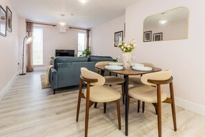 A modern living room with a sofa, a dining table with chairs, a TV, and a large mirror. - Toast Stays - The Bluebell at Parsons House (Washington)