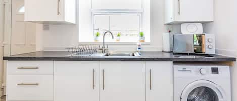 A modern kitchen with a built-in washing machine, a sink with a dish rack, and a window with potted plants.