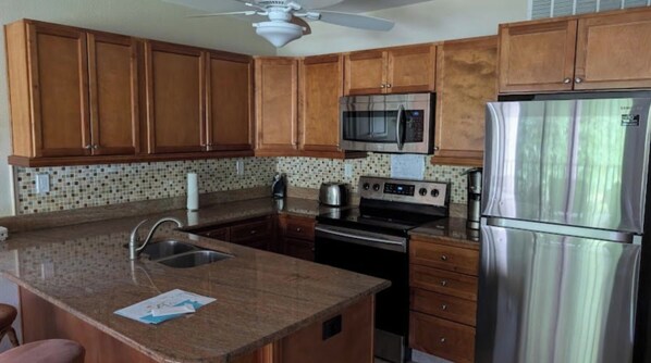 A kitchen with wooden cabinets, a stainless steel refrigerator, a microwave, and a stove. - 2-bedroom condo in serene Marco Island right on the beach (Marco Island)