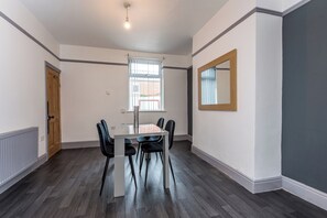 A dining area with a table and chairs, a window with blinds, and a door. - Toast Stays - Greenwell (Darlington)