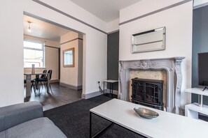 Un salon moderne avec une cheminée, un coin repas avec des chaises et une grande fenêtre.