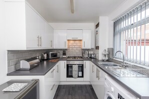 A modern kitchen with white cabinets, a built-in oven, a dishwasher, and a window with a view of the outside. - Toast Stays - Greenwell (Darlington)
