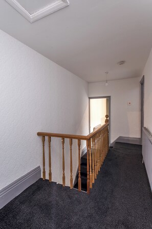A hallway with a wooden staircase, carpeted floor, and white walls. - Toast Stays - Greenwell (Darlington)