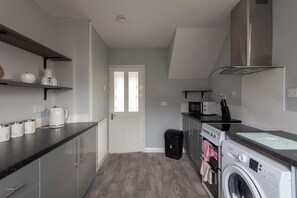 A compact kitchen with a washing machine, microwave, and a small oven. - Toast Stays - Larchcroft (Shildon)