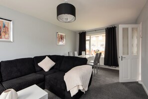 Ein modernes Wohnzimmer mit einem schwarzen Sofa, einem weißen Couchtisch und einem Essbereich mit Tisch und Stühlen.
