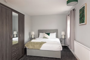 A bedroom with a bed, bedside tables, a wardrobe, and a radiator. - Toast Stays - Larchcroft (Shildon)