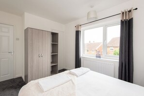 Ein Schlafzimmer mit einem Bett, einem Kleiderschrank, einem Fenster mit Vorhängen und einer Heizung.