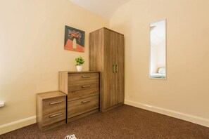 A room with a wardrobe, a small cabinet, a potted plant, and a framed picture on the wall. - Toast Stays - Church Street (Hill Top)