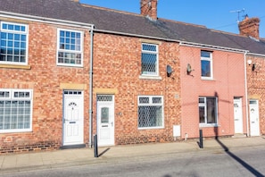 A two-story brick house with a white door, a window with a metal grill, and a satellite dish on the roof. - Toast Stays - Church Street (Hill Top)