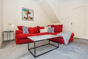 A red sofa with patterned cushions, a marble coffee table, a framed picture on the wall, a small side table, and a white door. - Toast Stays - Church Street (Hill Top)