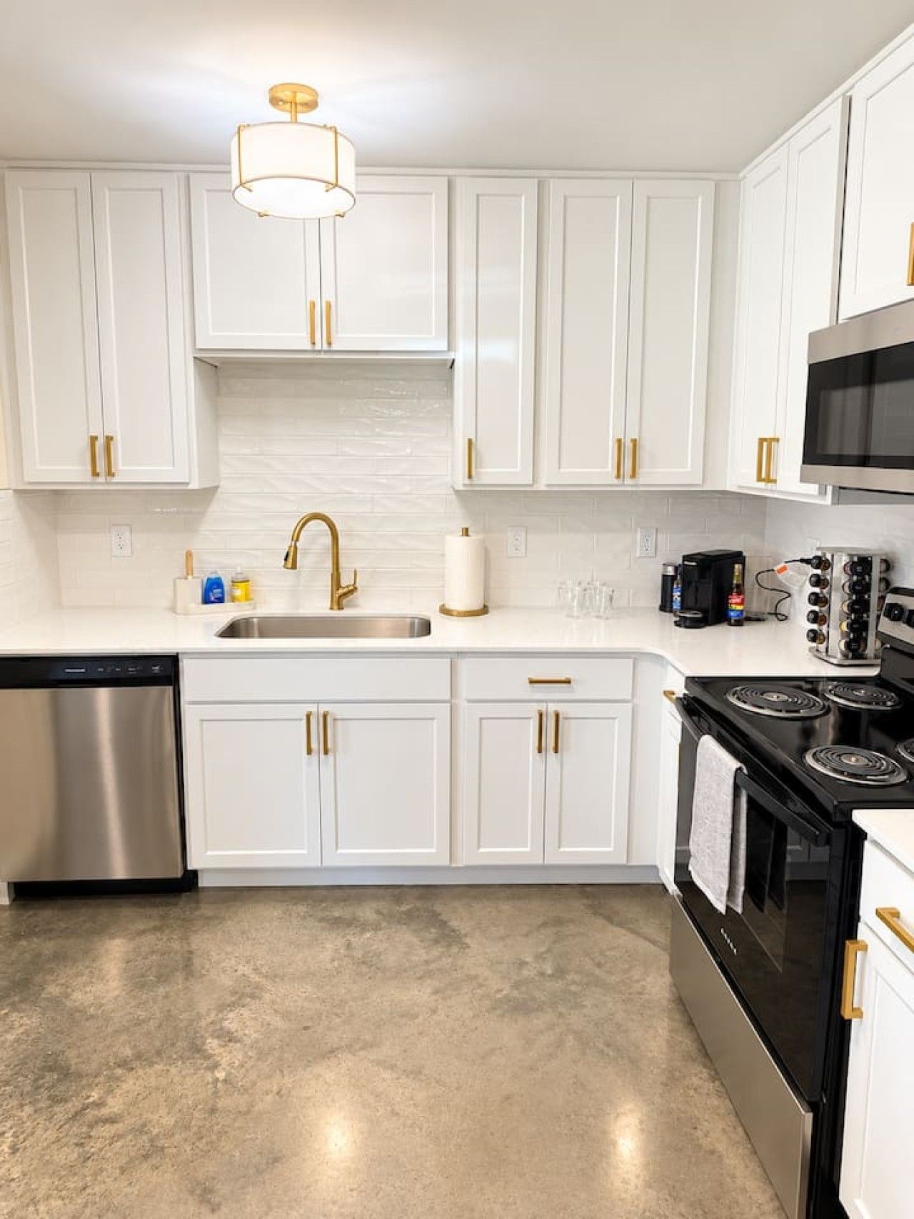 A modern kitchen with white cabinets, a stainless steel dishwasher, a black stove, and a microwave.