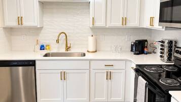A modern kitchen with white cabinets, a stainless steel dishwasher, a black stove, and a microwave.
