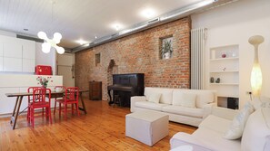 A living room with a brick wall, a sofa, a coffee table, a TV, and a dining area with a table and chairs. - Italianway Comfort - Agudio 8 (Milano)
