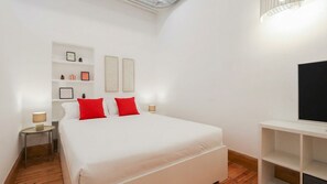 Habitació d'hotel amb un llit, taules de nit, un televisor i una estant amb quadres emmarcats.