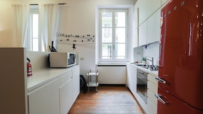 A compact kitchen with a microwave, a small cart, and a red refrigerator. - Italianway Comfort - Agudio 8 (Milano)