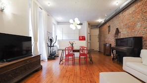 A modern living room with a flat-screen TV, a dining area with red chairs, and a brick wall. - Italianway Comfort - Agudio 8 (Milano)