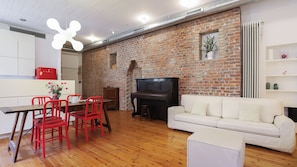A living room with a brick wall, a piano, a white sofa, and red chairs. - Italianway Comfort - Agudio 8 (Milano)