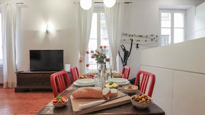 A dining area with a wooden table, red chairs, a TV, and a wall with a bird mural. - Italianway Comfort - Agudio 8 (Milano)