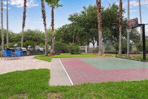 An outdoor basketball court with a green and red surface, surrounded by palm trees and a barbecue area. - Hawthorn Suites Suite Near Universal Orlando (Orlando)