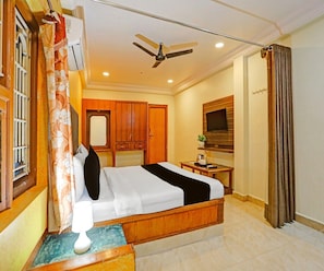 Una habitación de hotel con cama, escritorio, televisor y ventilador de techo.