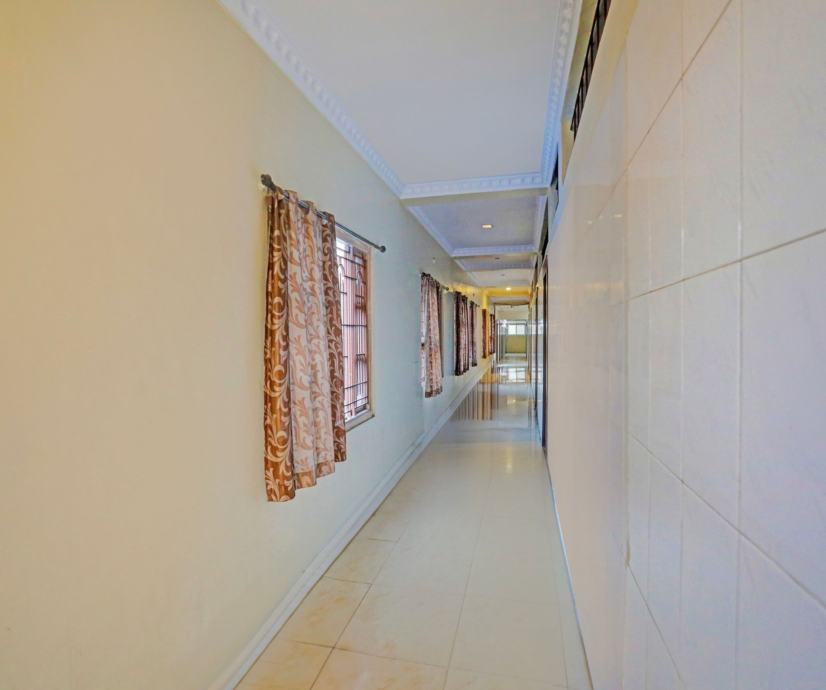 A long, narrow hallway with patterned curtains on the left, a tiled floor, and a plain wall on the right.