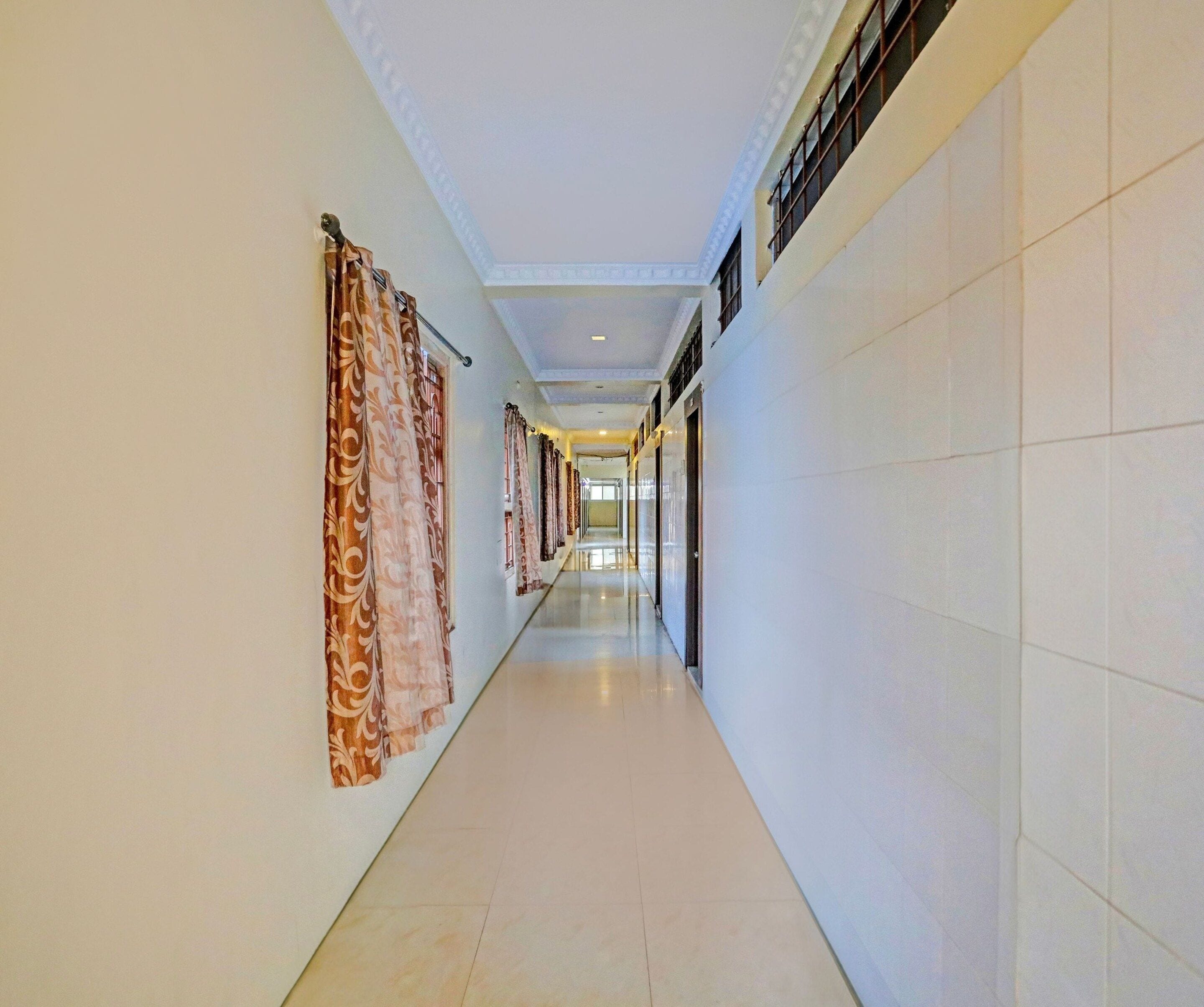 A long, narrow hotel corridor with patterned curtains on one side and plain walls on the other.