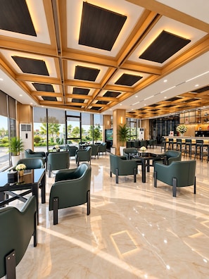 A modern hotel lobby with a geometric ceiling design, marble flooring, and green upholstered seating. - H Hotel & Apartments (Hai Phong)