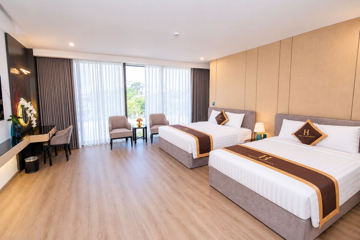 Habitación de hotel con dos camas, un escritorio, sillas y vistas amplias por los ventanales.