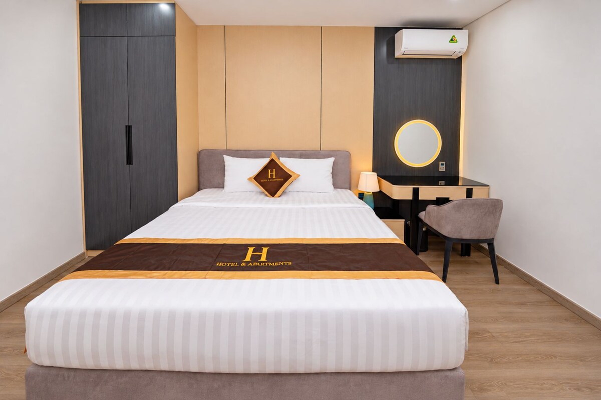 Habitación de hotel con cama, escritorio, silla, armario y equipo de aire acondicionado.