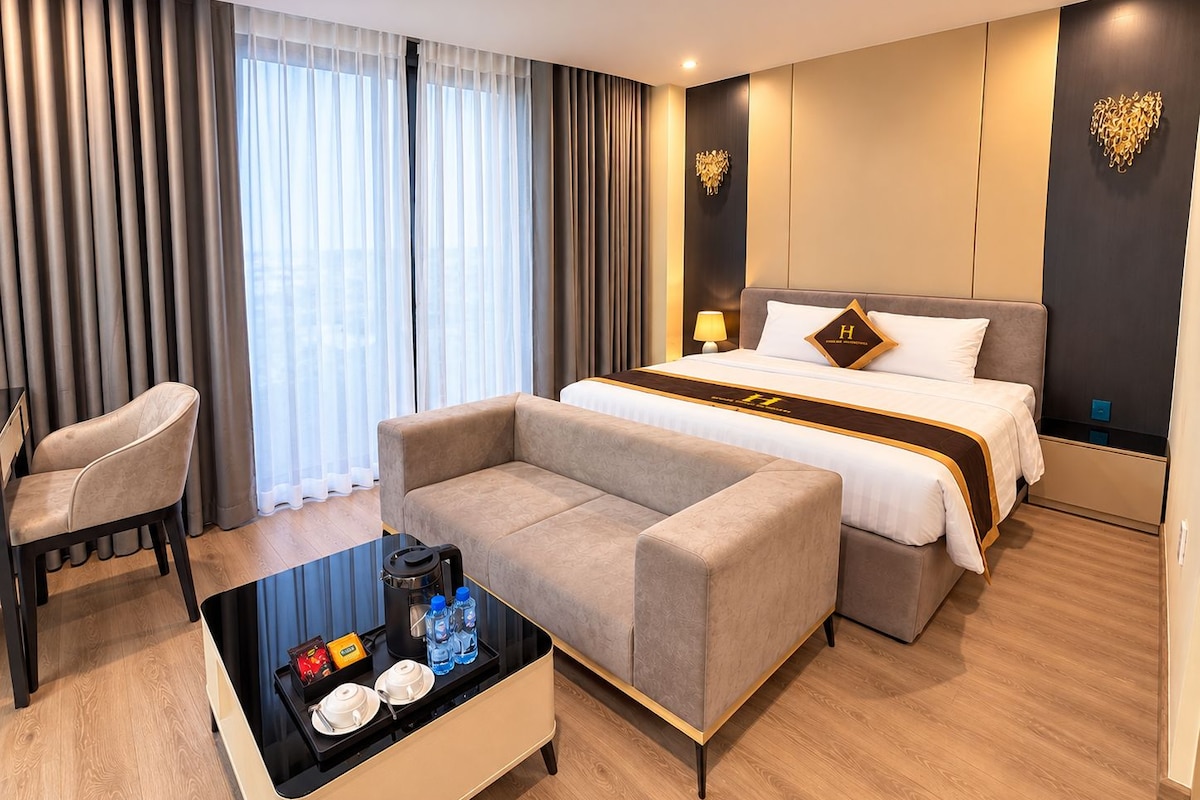 A hotel room with a bed, sofa, and a coffee table with amenities.