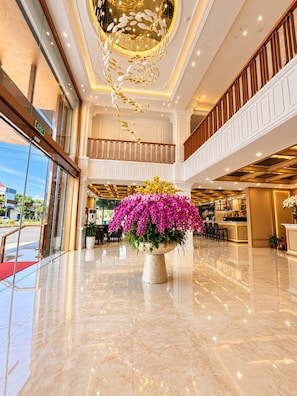 A hotel lobby with a marble floor, a large floral centerpiece, and a modern chandelier. - H Hotel & Apartments (Hai Phong)