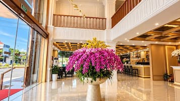 A hotel lobby with a marble floor, a large floral centerpiece, and a modern chandelier.