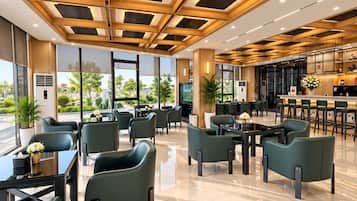 A modern hotel lobby with a geometric ceiling design, marble flooring, and green upholstered seating.