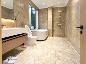 A modern bathroom with a marble floor, a freestanding toilet, a bathtub, and a shower. - H Hotel & Apartments (Hai Phong)