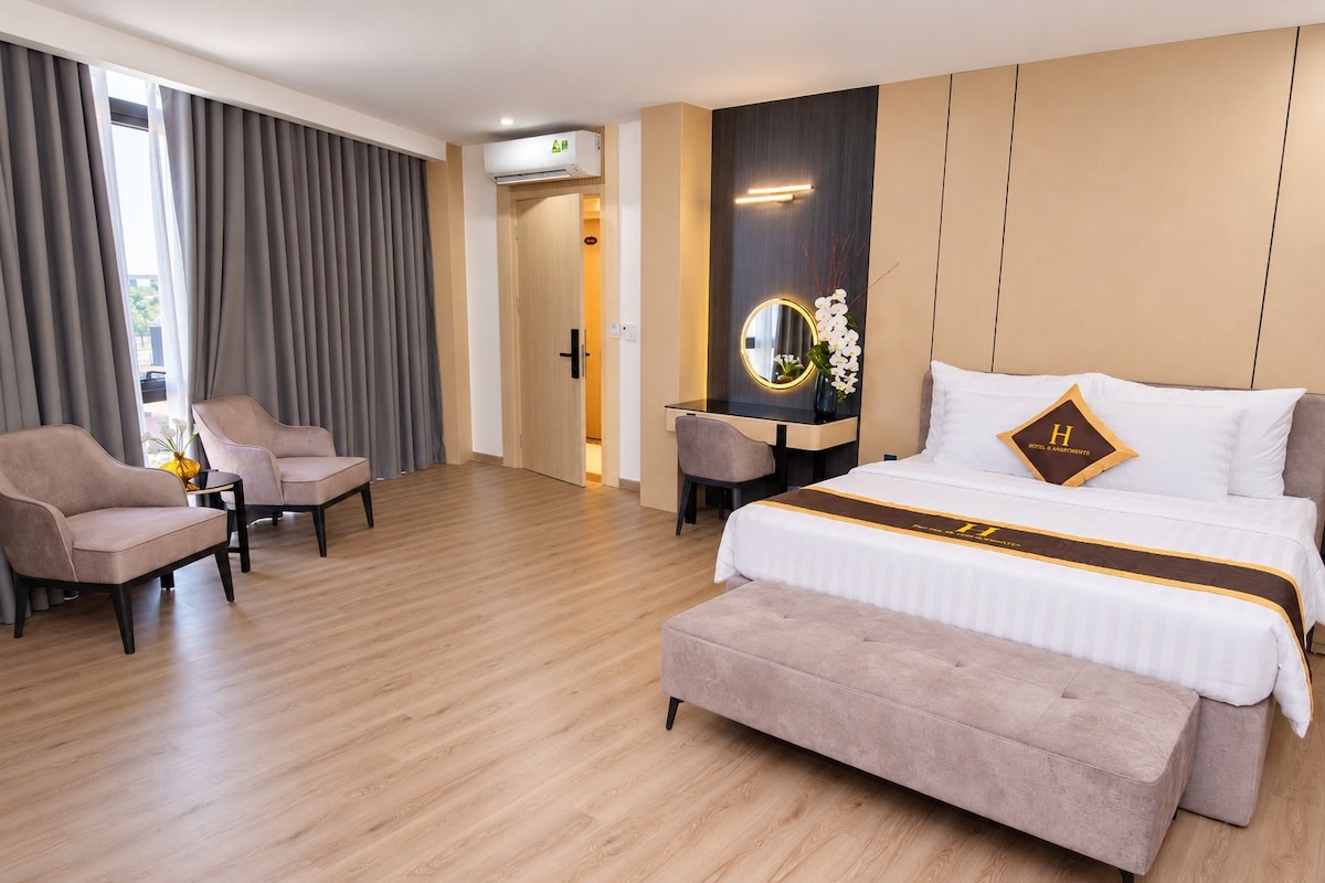 Una habitación de hotel con una cama, dos sillones, un escritorio y un espejo.