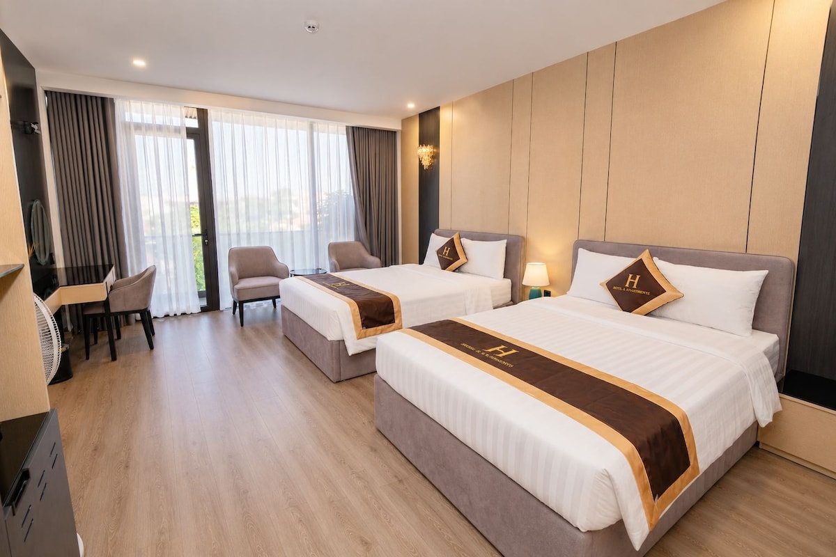 Habitación de hotel con dos camas, un escritorio, sillas y vistas al exterior.