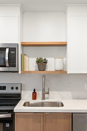 A kitchen with white cabinets, a stainless steel sink, a microwave, an oven, and a wooden countertop. - Simple & Modern Stay in Houston (Houston)