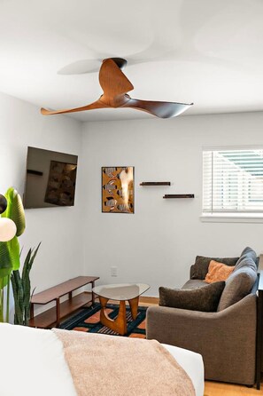 Uma sala de estar moderna com um ventilador de teto, um sofá, uma mesa de centro e obras de arte nas paredes.