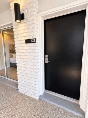 A modern building entrance with a white brick wall, a black door, and a number sign '101'. - Good Tides at 300 Tenth | 101 (Myrtle Beach)