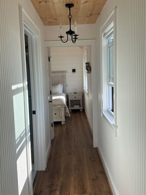 A narrow hallway with wooden flooring, white walls, a bed with a white headboard, a bedside table, and a nightstand. - 34 acre Retreat Mountain View hiking trails King 1bedroom 23 mins to Cleveland (Calhoun)