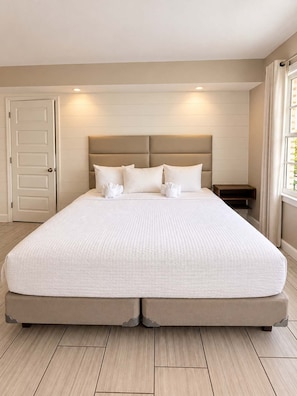 A large bed with a headboard, a bedside table, and a window with curtains. - The Coastal Pearl at 300 Tenth | 217 (Myrtle Beach)
