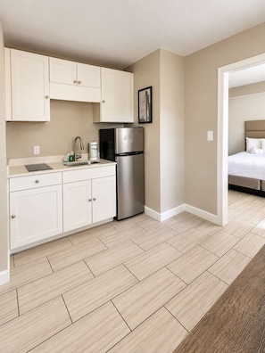 A compact kitchen with white cabinets, a stainless steel refrigerator, and a tiled floor. - The Coastal Pearl at 300 Tenth | 217 (Myrtle Beach)