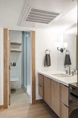 Ein modernes Badezimmer mit einem weißen Waschbecken, Holzschränken, einer Duschkabine aus Glas und einem Spiegel mit Wandleuchten.