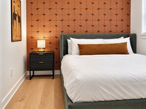 A bedroom with a bed, a nightstand, a lamp, and a wall with a patterned design. - Central Houston Retreat | Sleeps 4 | Richmond Ave (Houston)