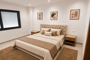 A bedroom with a large bed, two bedside tables, a window with blinds, and three framed artworks on the wall. - Peaceful Garden (Tunis)